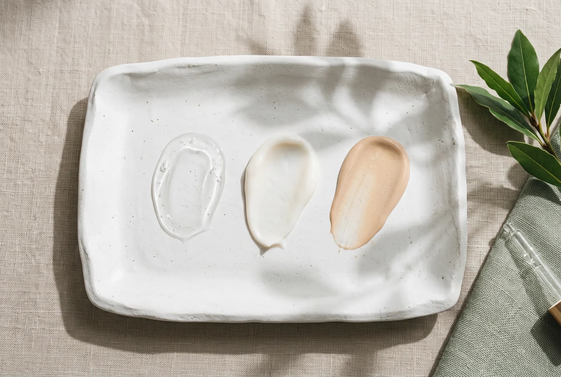 Clear serum, lotion, and sheer tinted sunscreen textures shown on a ceramic tray