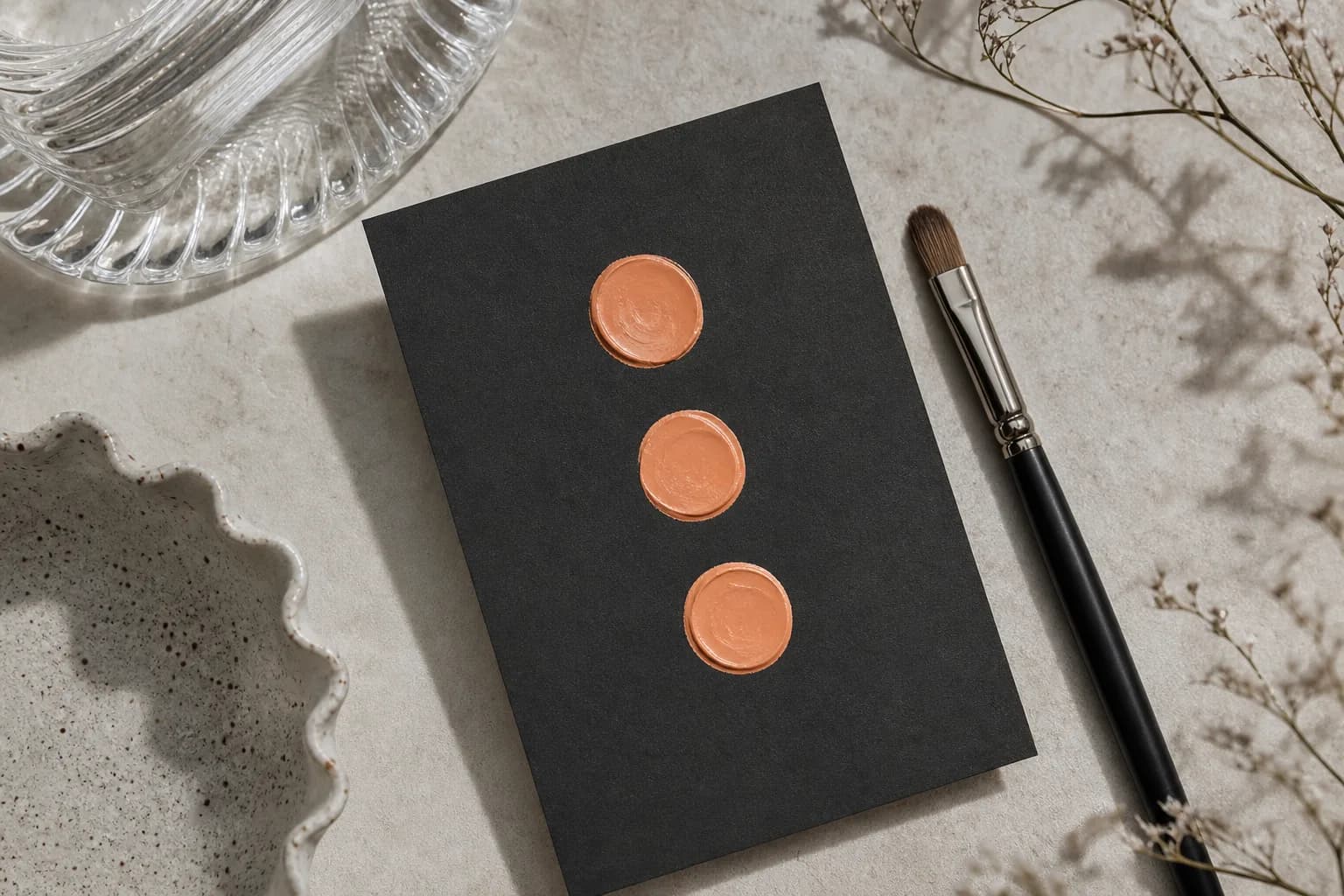 Swatches of peach/orange correctors on a black card with a small brush