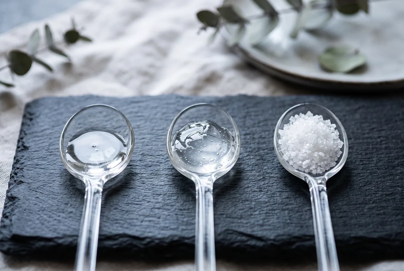 Three spoons showing humectant textures: glycerin, HA gel, urea crystals
