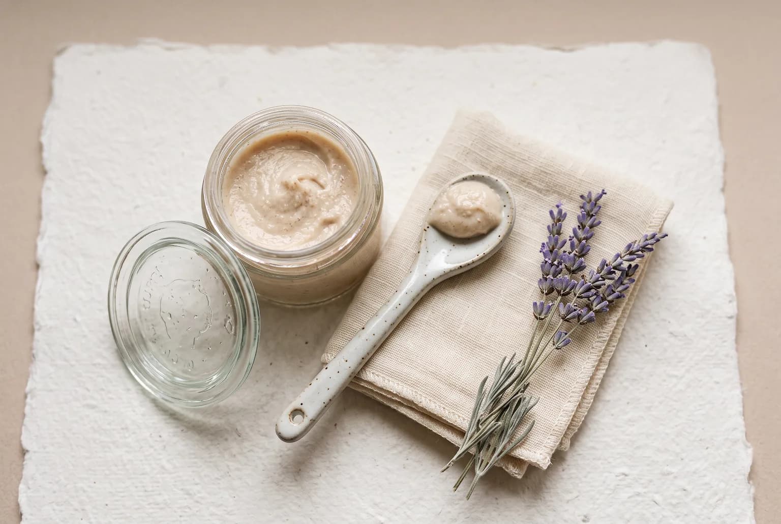 Still life of gentle skincare tools and soft cloth near a jar of cream on pale background