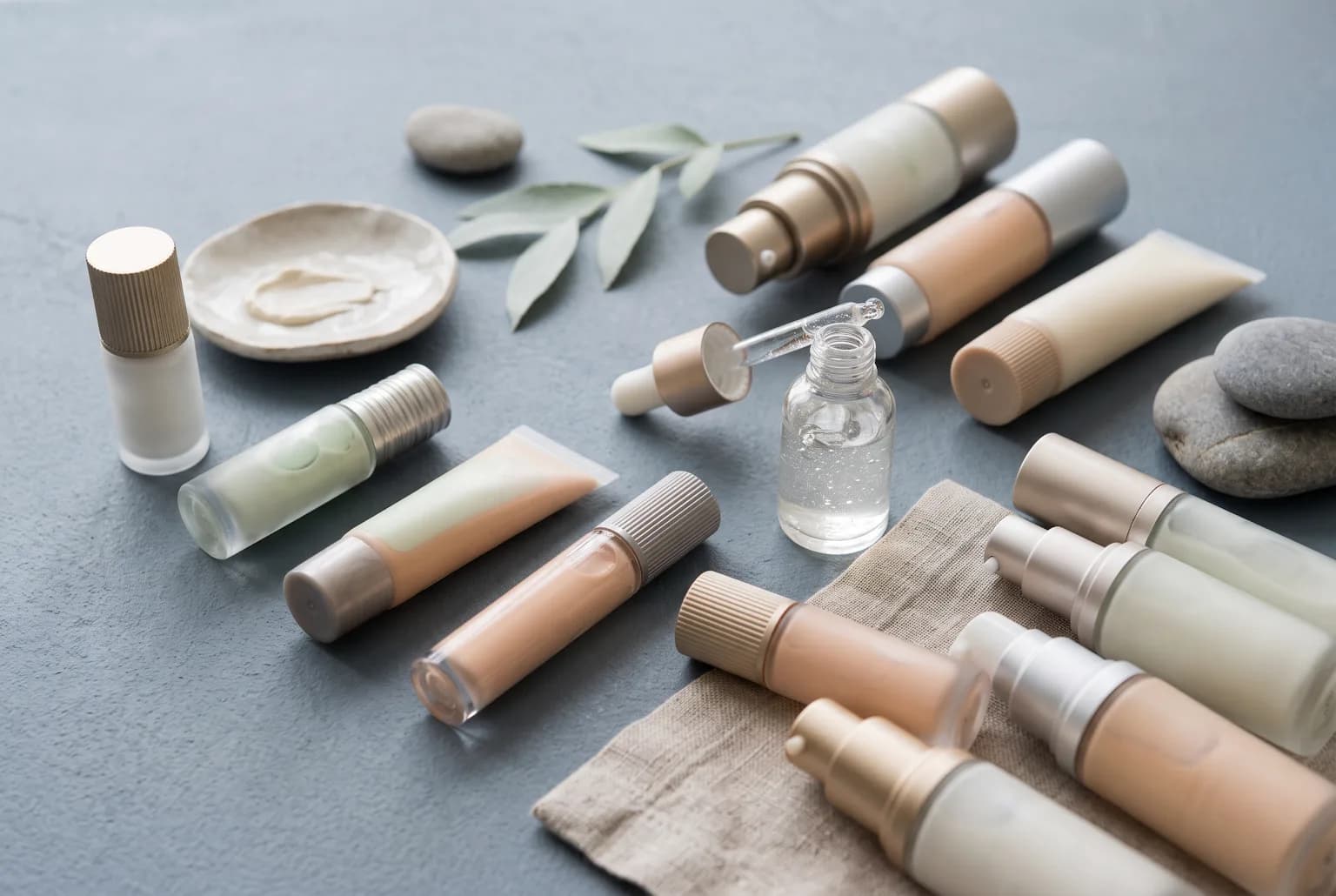 Primers, color corrector tubes and silicone-hybrid drops flat lay, pastel background
