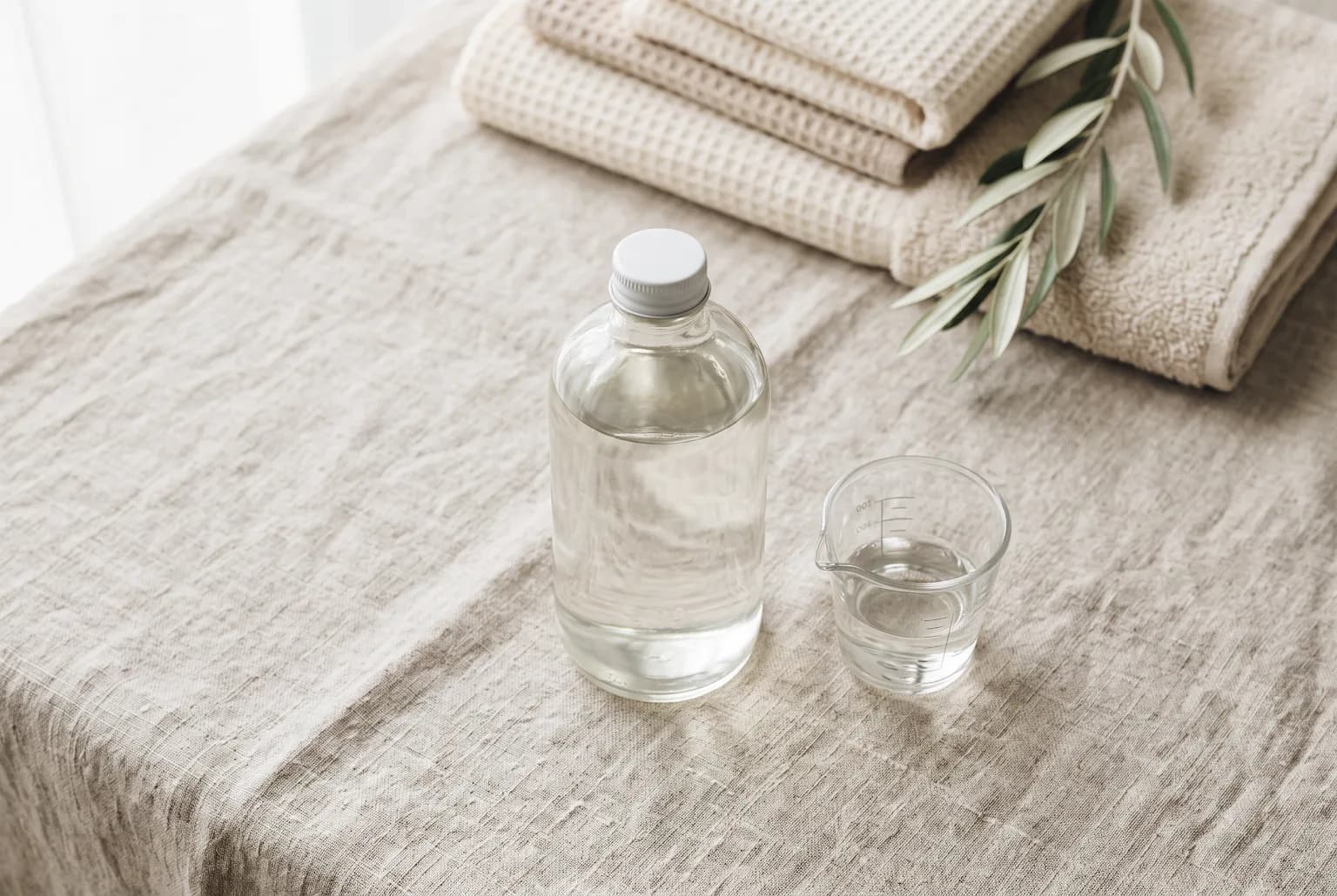 Editorial hero: fragrance-free detergent bottle and folded cotton towels, soft window light