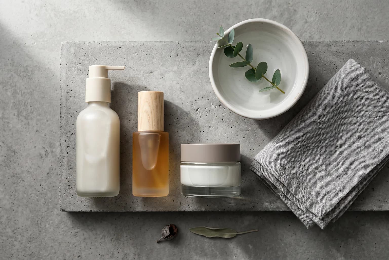 Overhead still life of cleanser, SPF, and moisturizer on concrete with towel