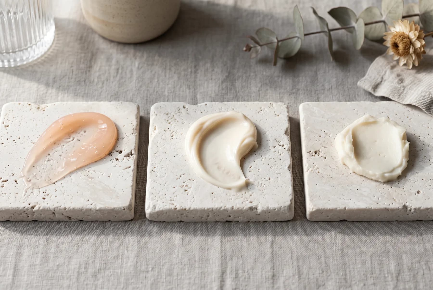 Three moisturizer textures showing gel, cream, and balm consistencies on stone tiles