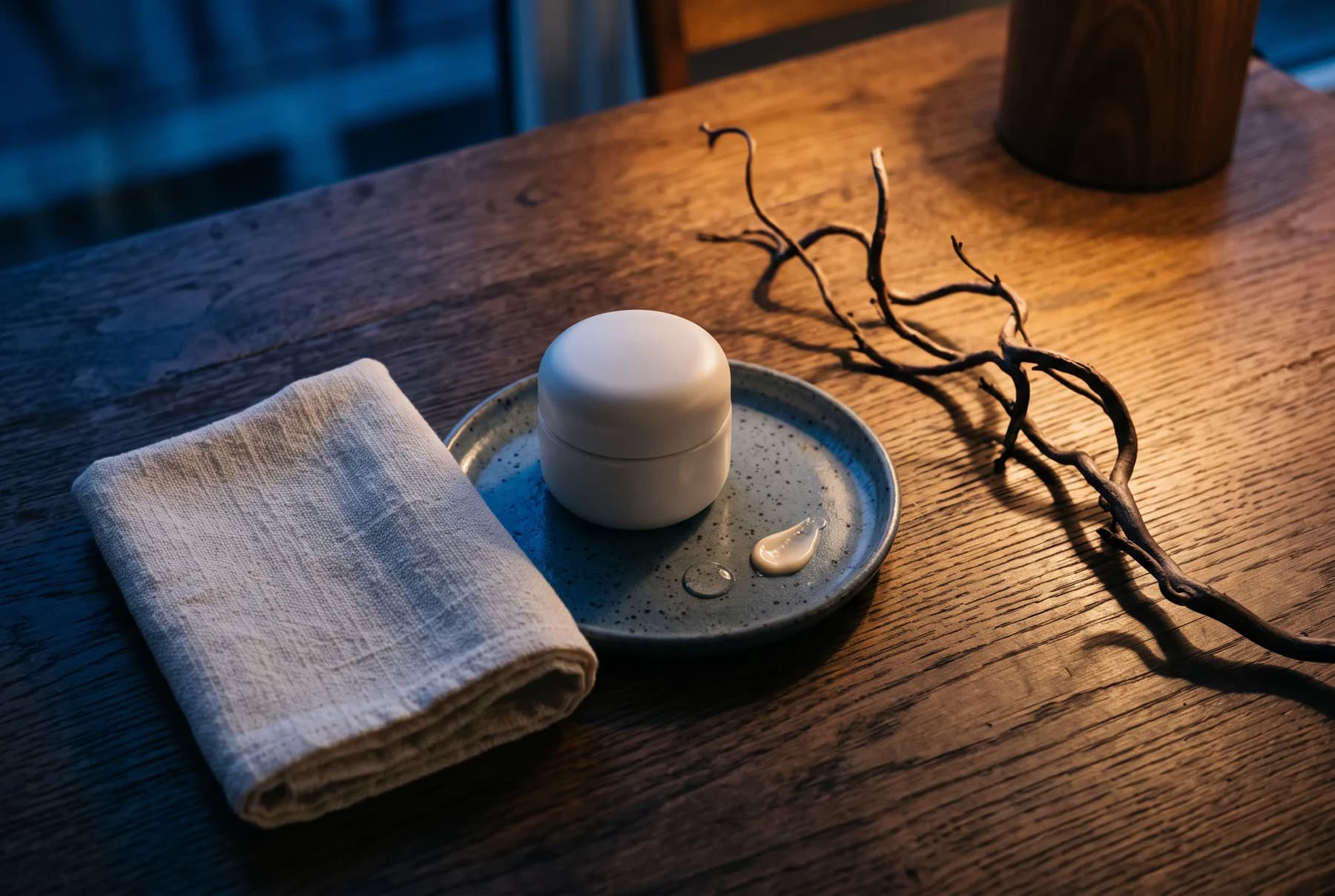 Moody nighttime skincare setting with a ceramic tray and washcloth