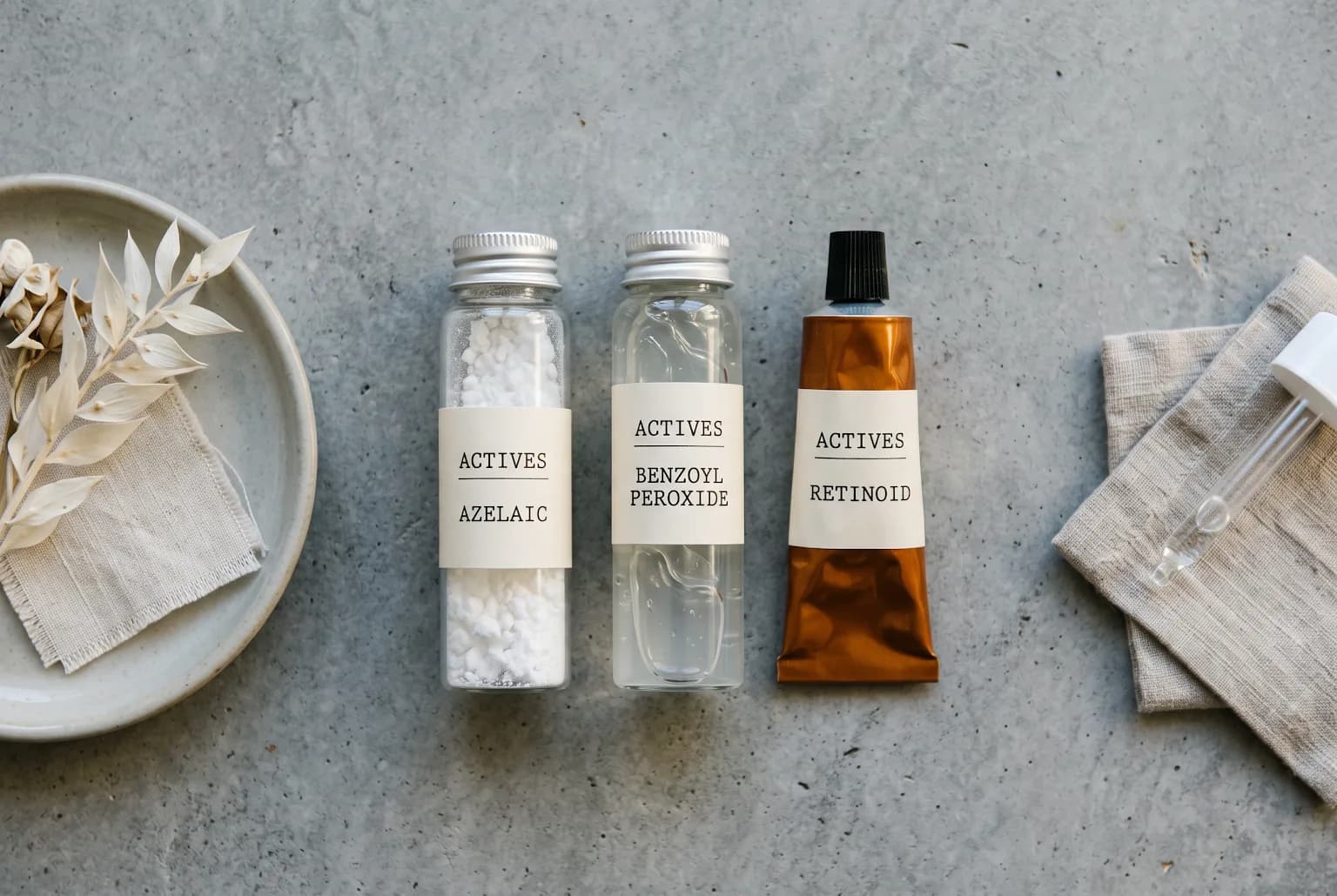 Three generic vials representing azelaic acid, benzoyl peroxide wash, and topical retinoid on grey background