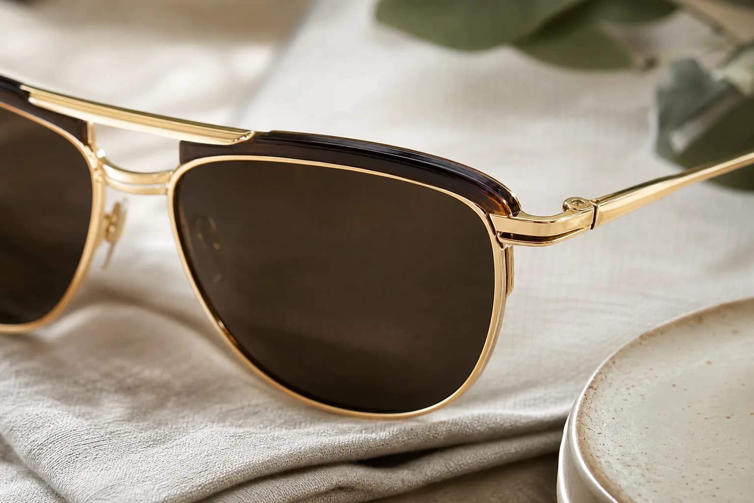 Close-up of gold-framed sunglasses with dark lenses resting on pale linen.