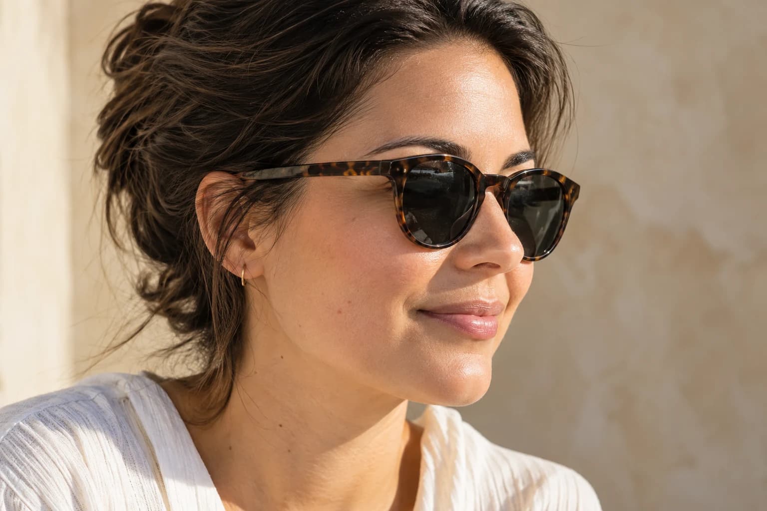 Three-quarter portrait of a woman wearing tortoiseshell sunglasses in sunlight.