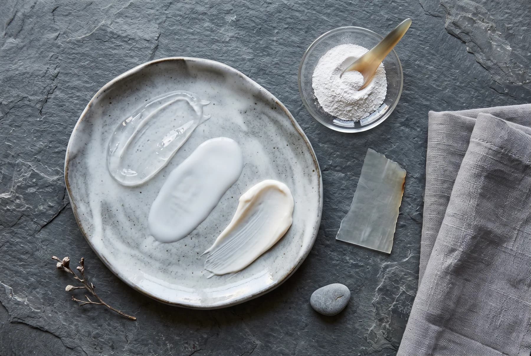 Clear gel, milky fluid, and cream sunscreen textures arranged on a ceramic palette