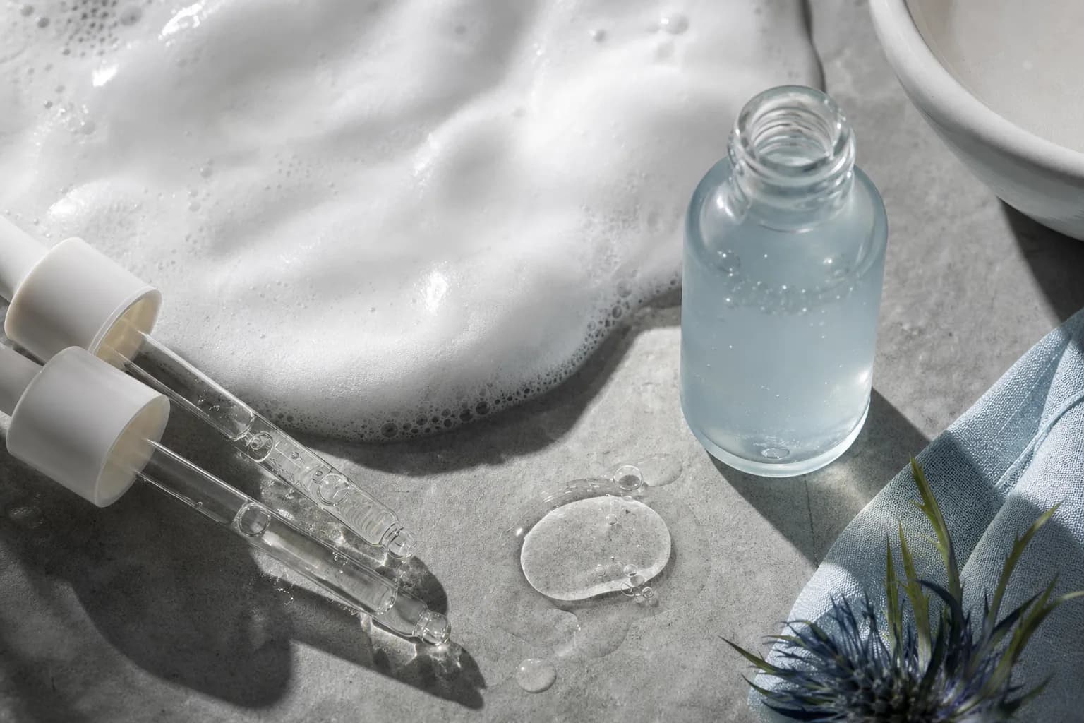 Lightweight serum droppers beside foamy cleanser puddle