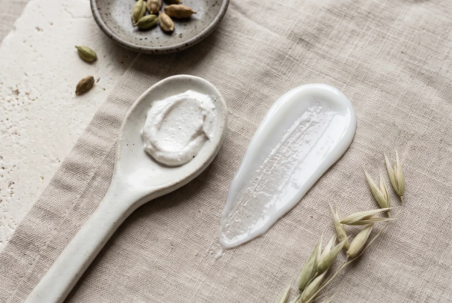 Sunscreen textures: mineral cream on ceramic spoon and lightweight lotion smear with neutral backdrop