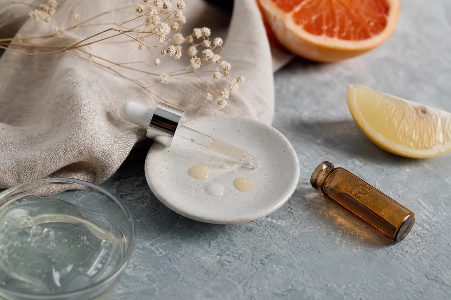 Flat-lay still life: glass dropper, amber ampoule and citrus slice on slate