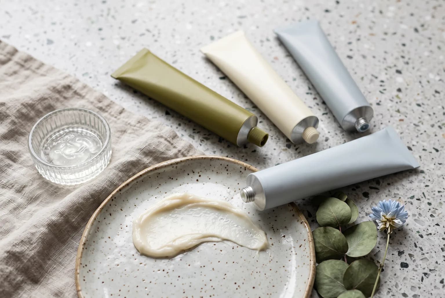 Tubes and an open balm on terrazzo showing thick creamy texture