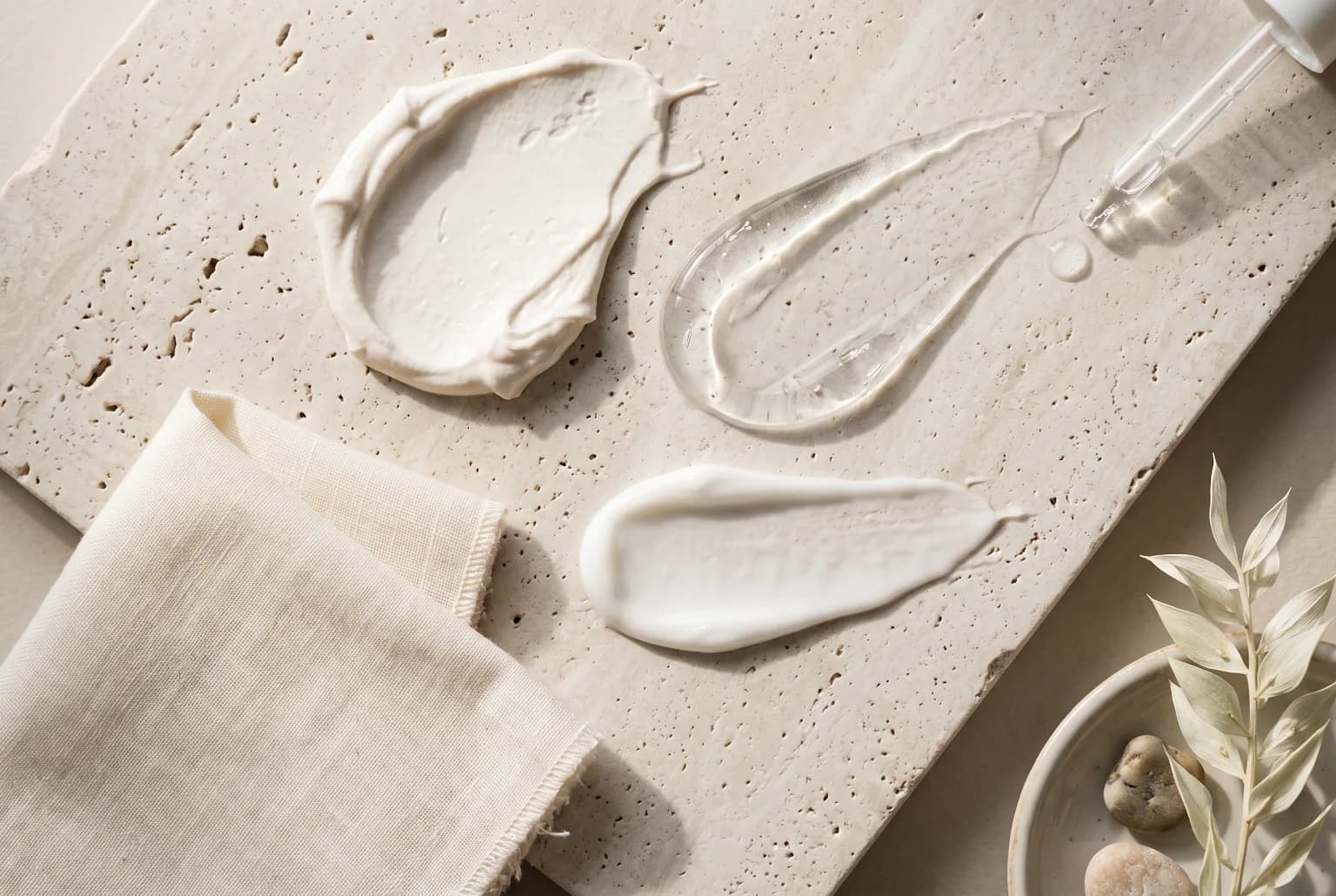 Cream, gel, and sunscreen textures arranged on pale stone