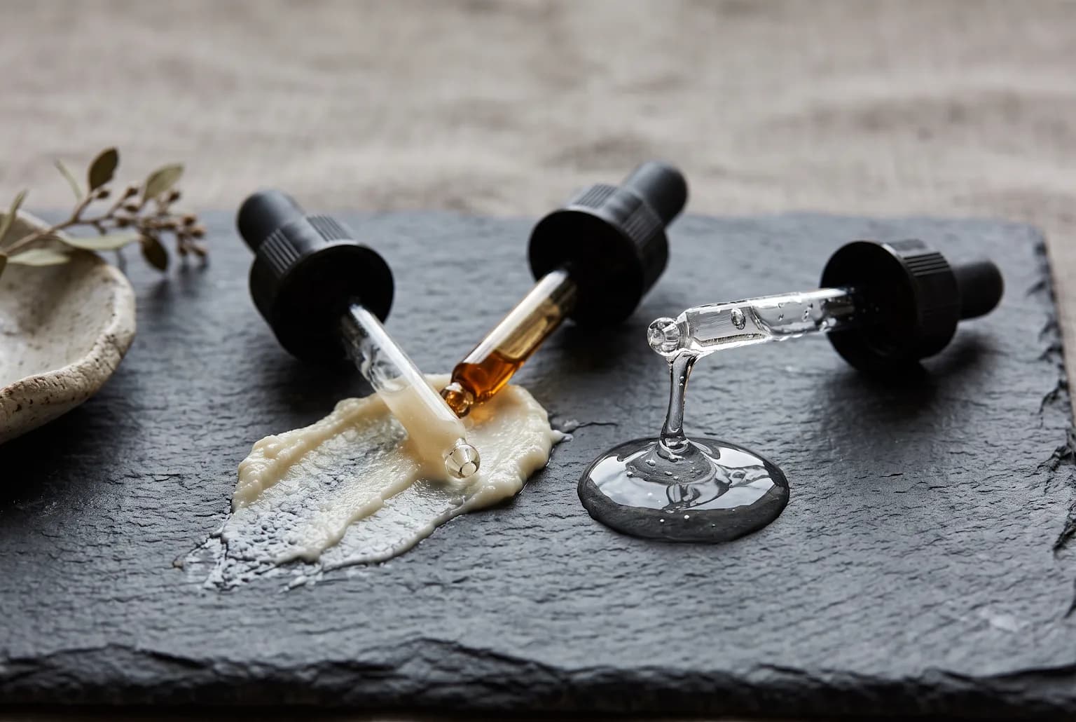 Three droppers on slate with visible gel strands and ceramide-rich cream smear, macro detail
