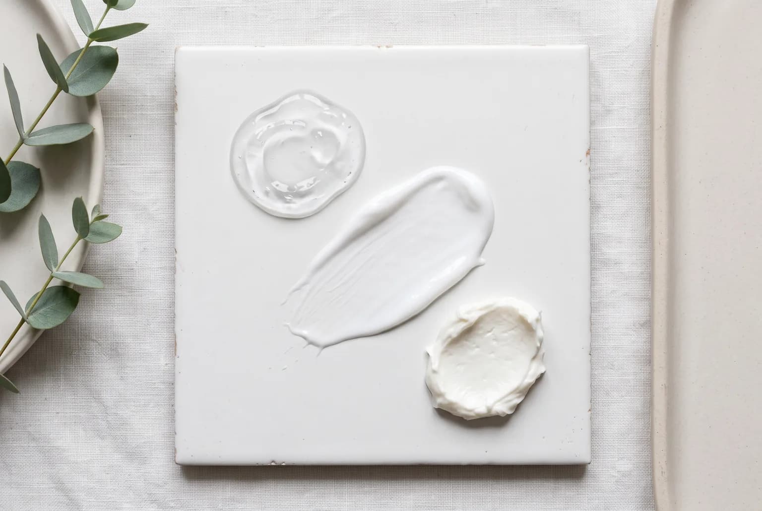 Three moisturizer textures—gel, lotion, cream—on a ceramic tile