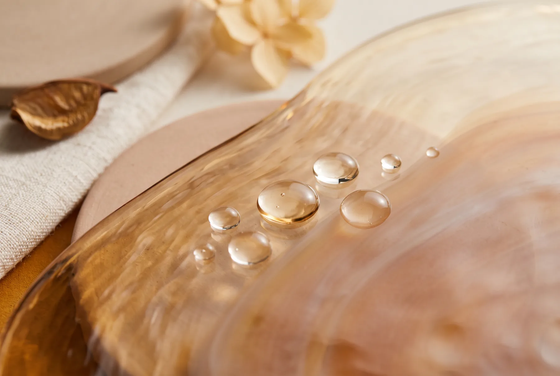 Editorial still life of translucent serum droplets and warm amber glass casting soft shadows